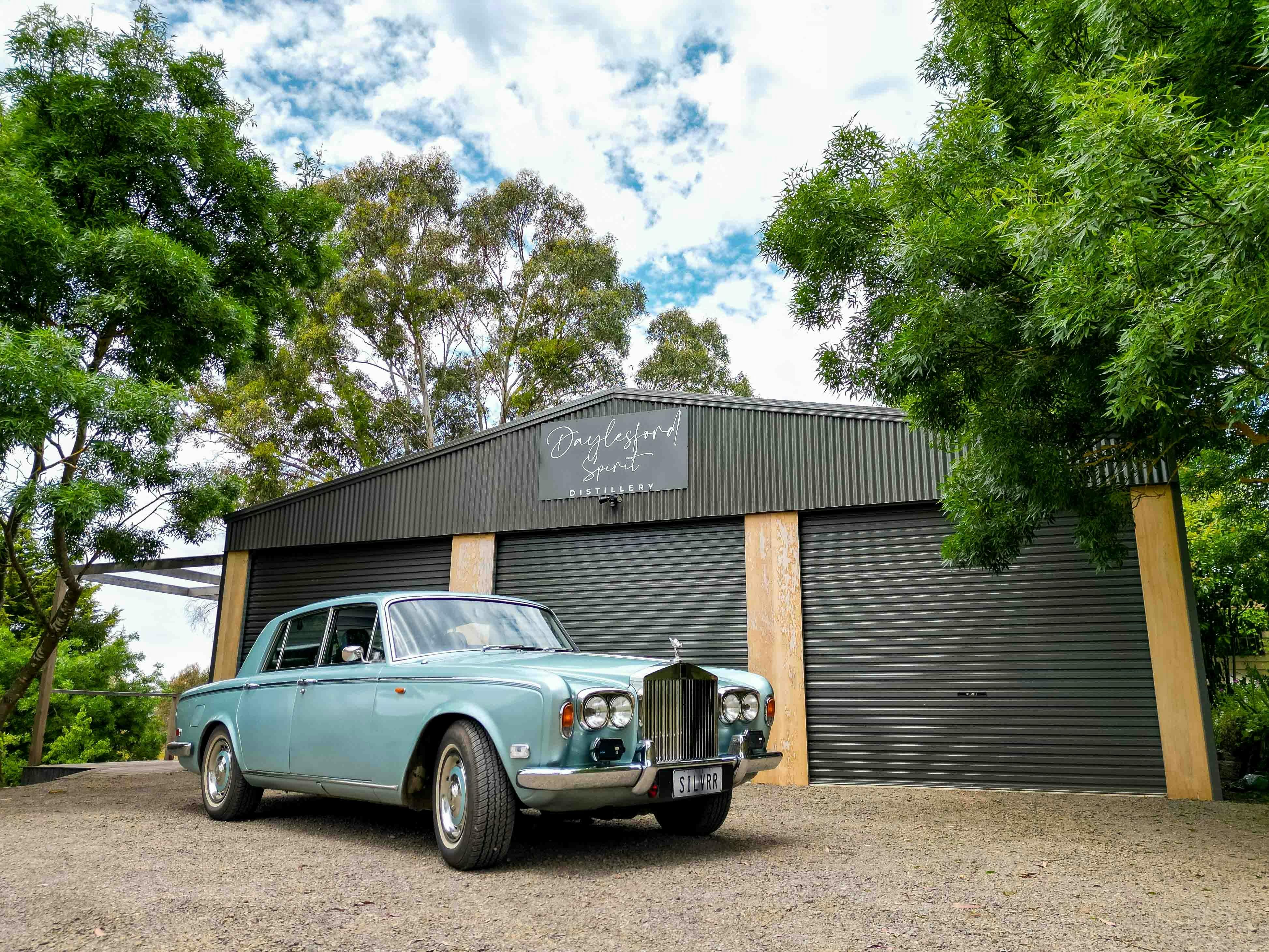 silver-blue vintage Rolls Royce parked under the "Daylesford Spirit" distillery sign