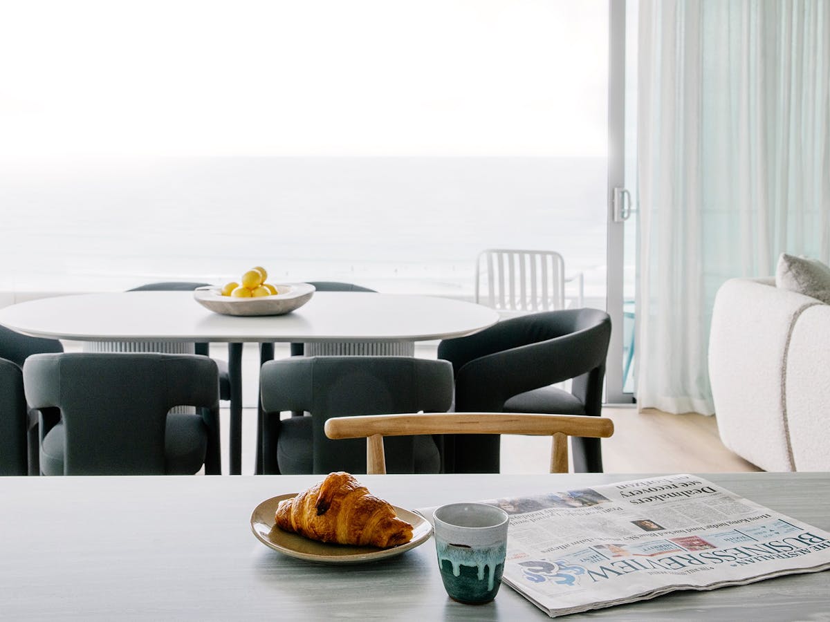 Relaxed Kirra Point breakfast setup with ocean views, croissant, coffee, and morning newspaper.