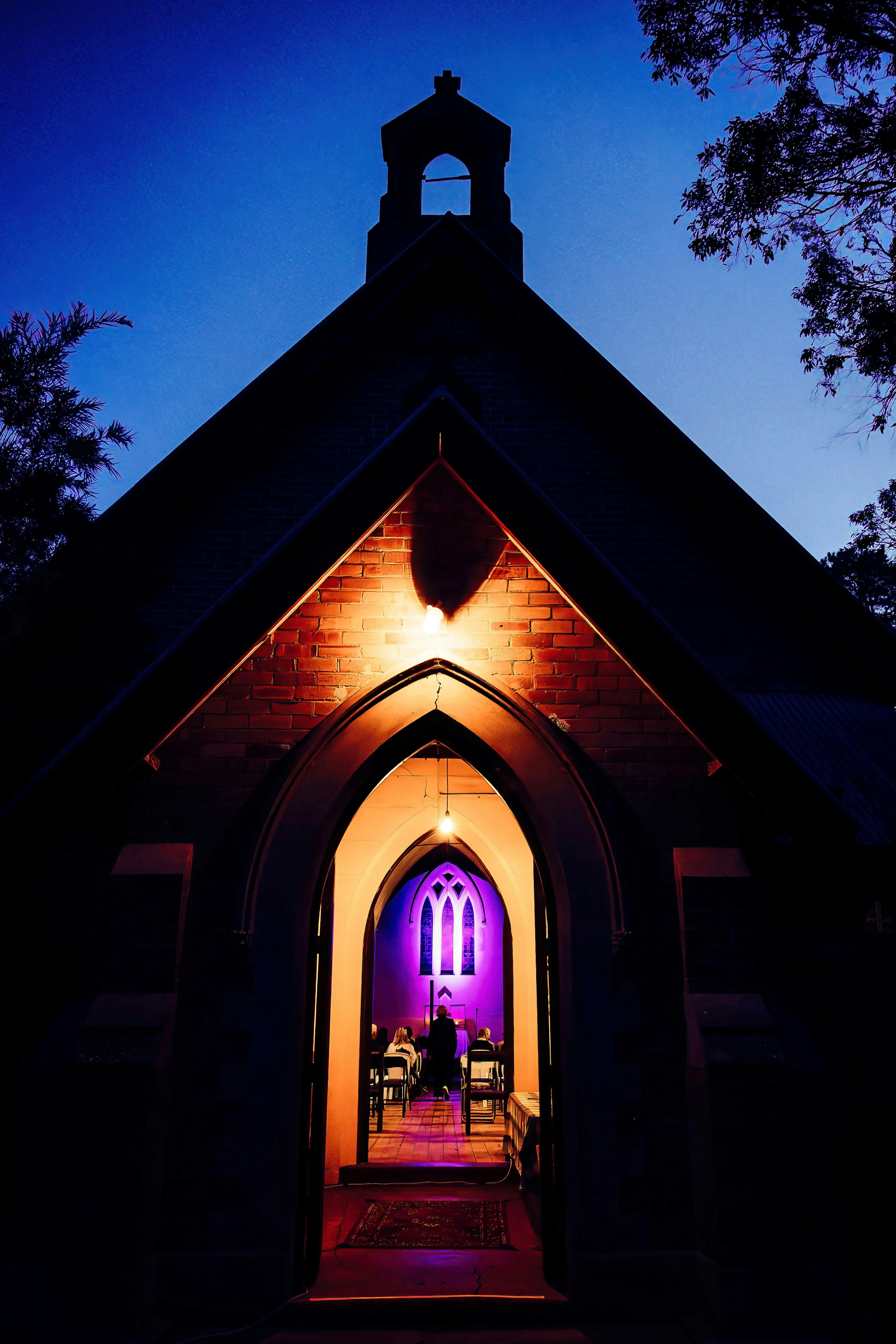 It is nighttime and the door of the church is illuminated in purple showing the arched windows