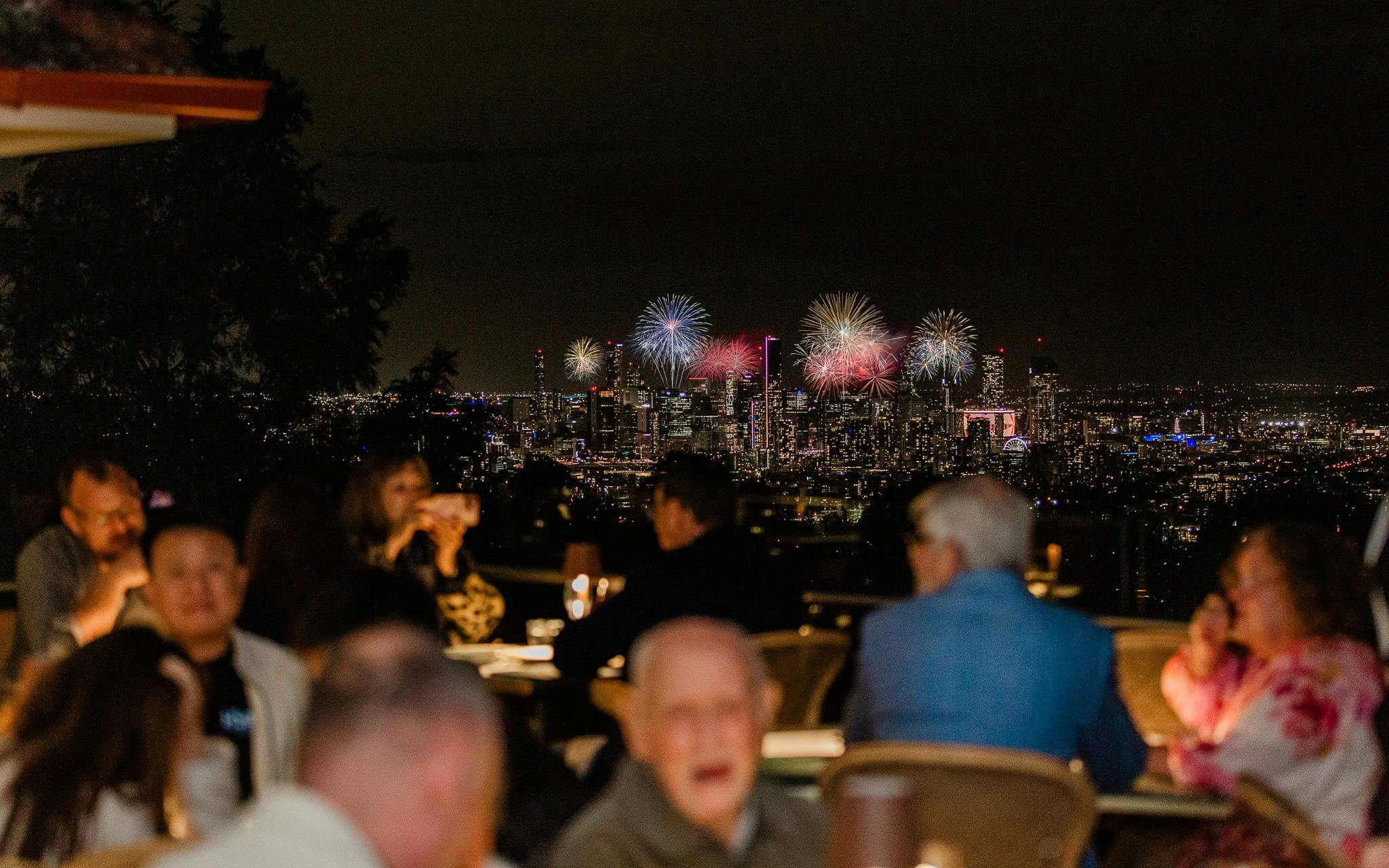 People dining with view of fireworks behind them