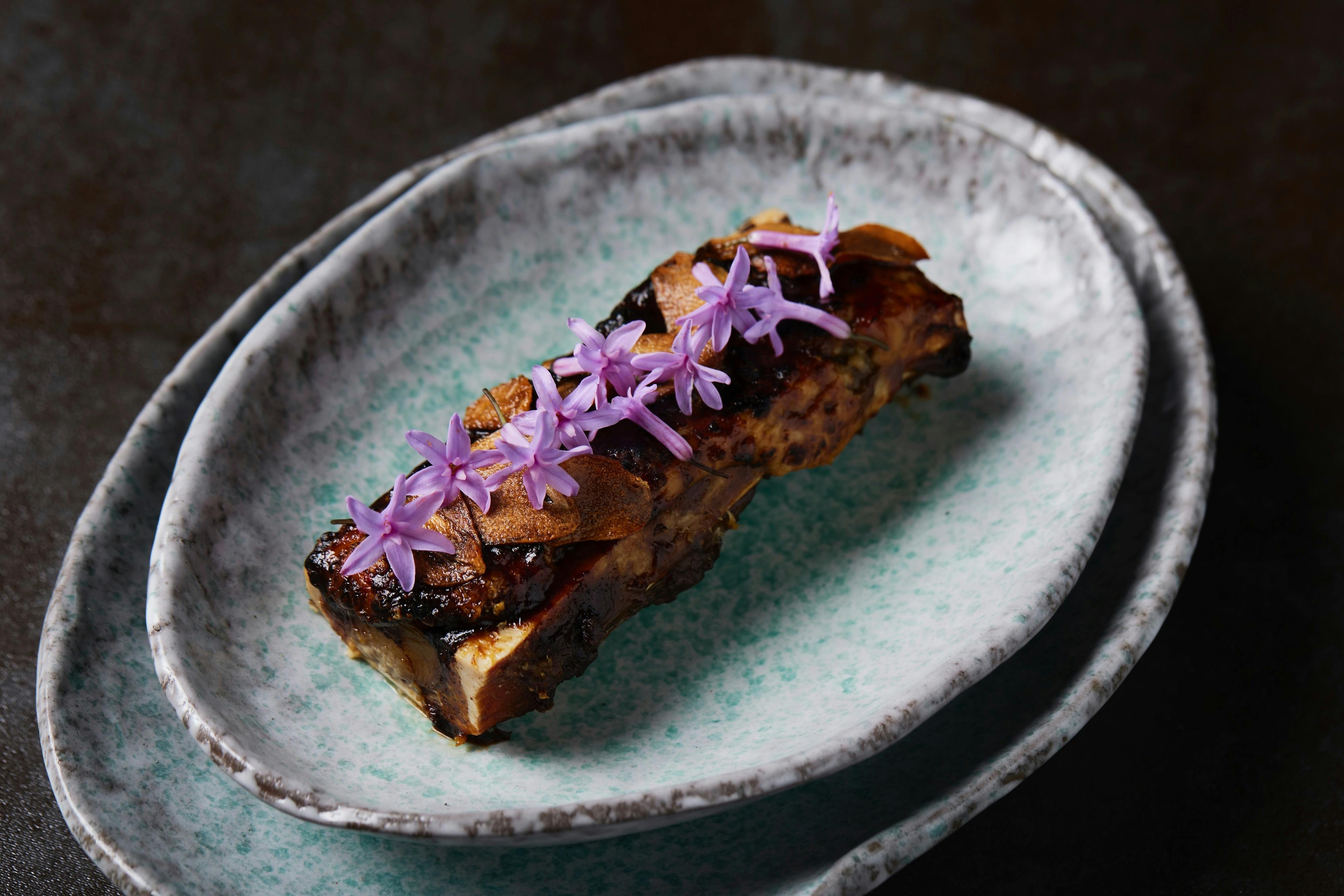 Image of a piece of cooked bone marrow with beautiful purple garlic flowers on top