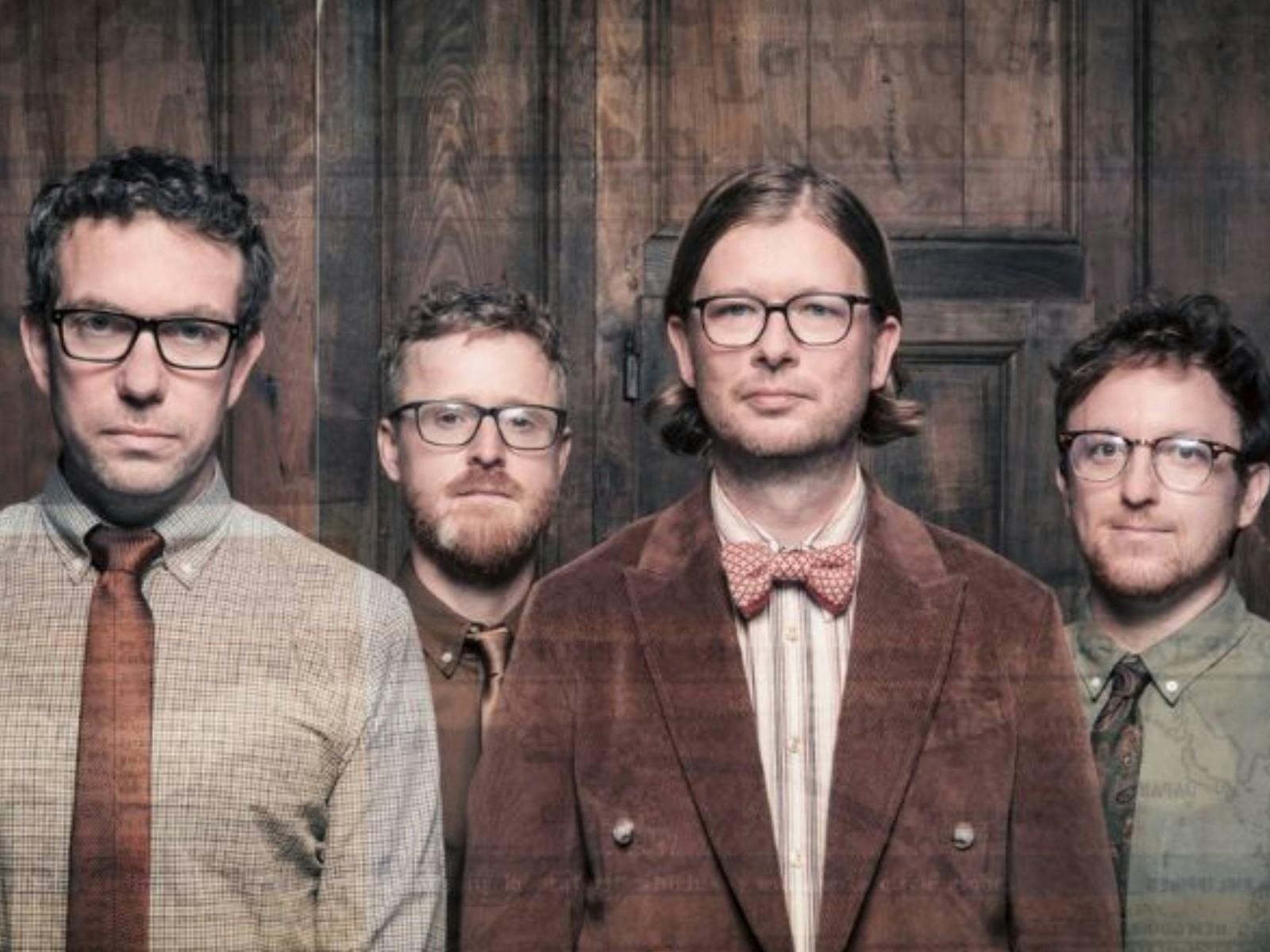 Four men wearing glasses, standing right next to eachother and looking directly at camera.