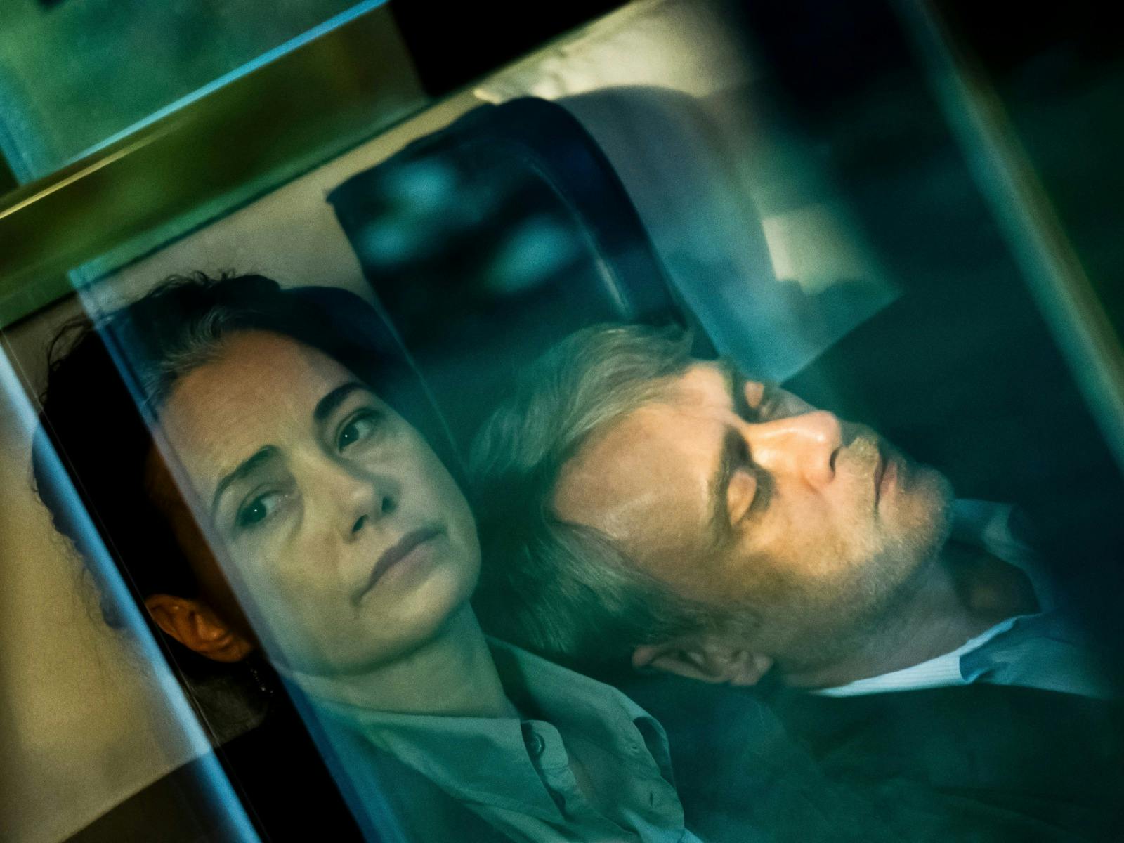 Hazy photo of woman looking morose past the camera and a man leaning on her shoulder