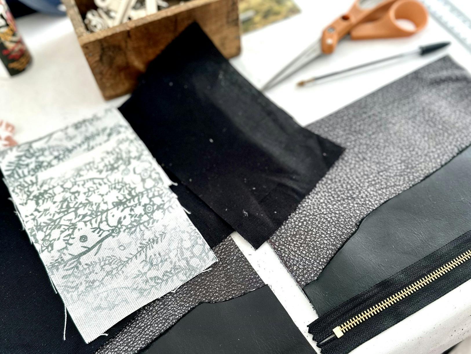 able setup for a leather workshop featuring fabric pieces, leather swatches, a zipper, scissors, a w