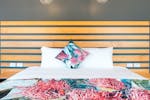 Queen bed with white sheets and pink floral doona and pillow with a wooden headrest