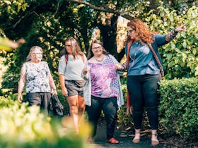 Four women walking through green garden looking at plants