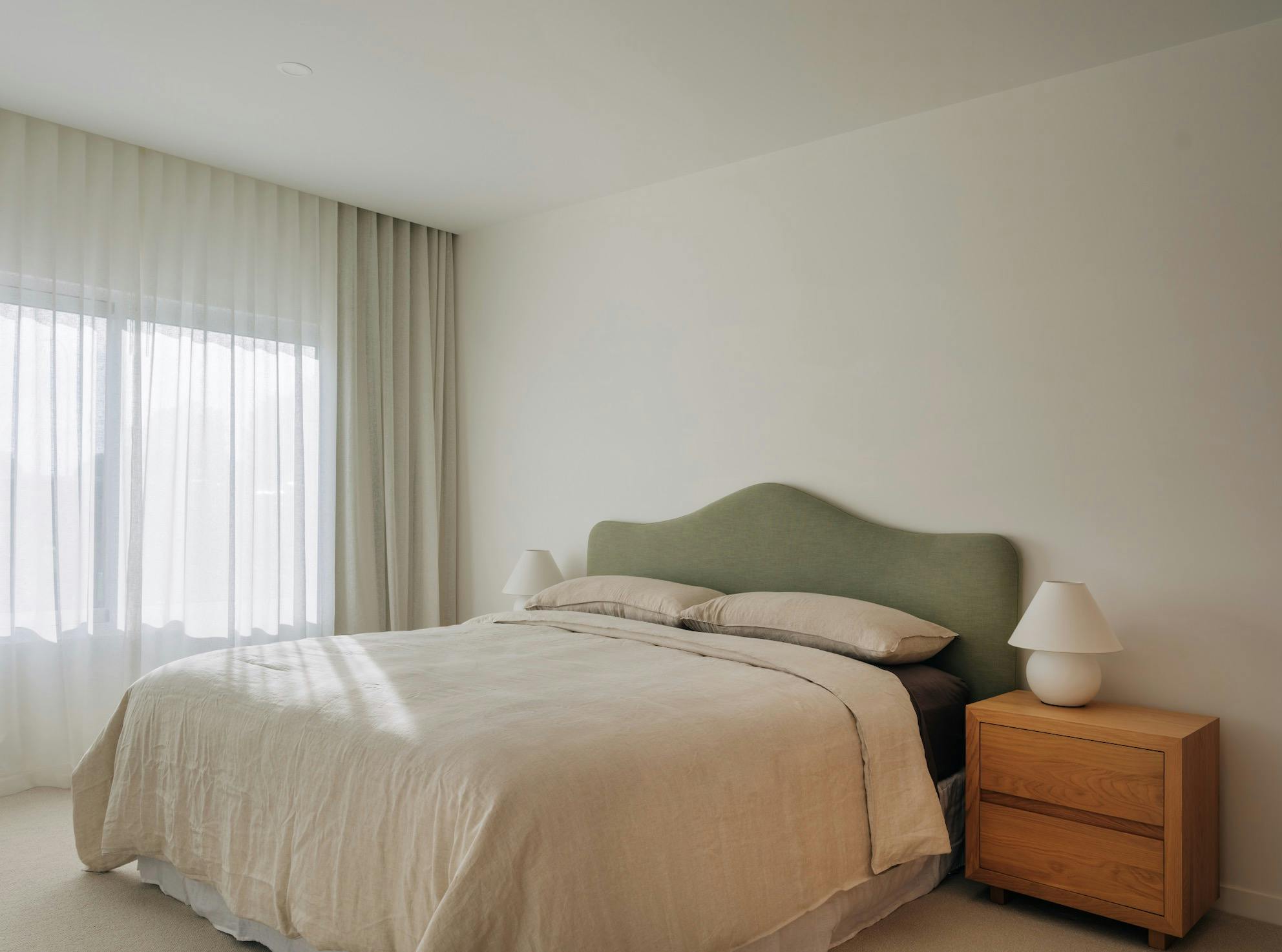 King size bed with green bed head, bedside tables and nice linen bedding