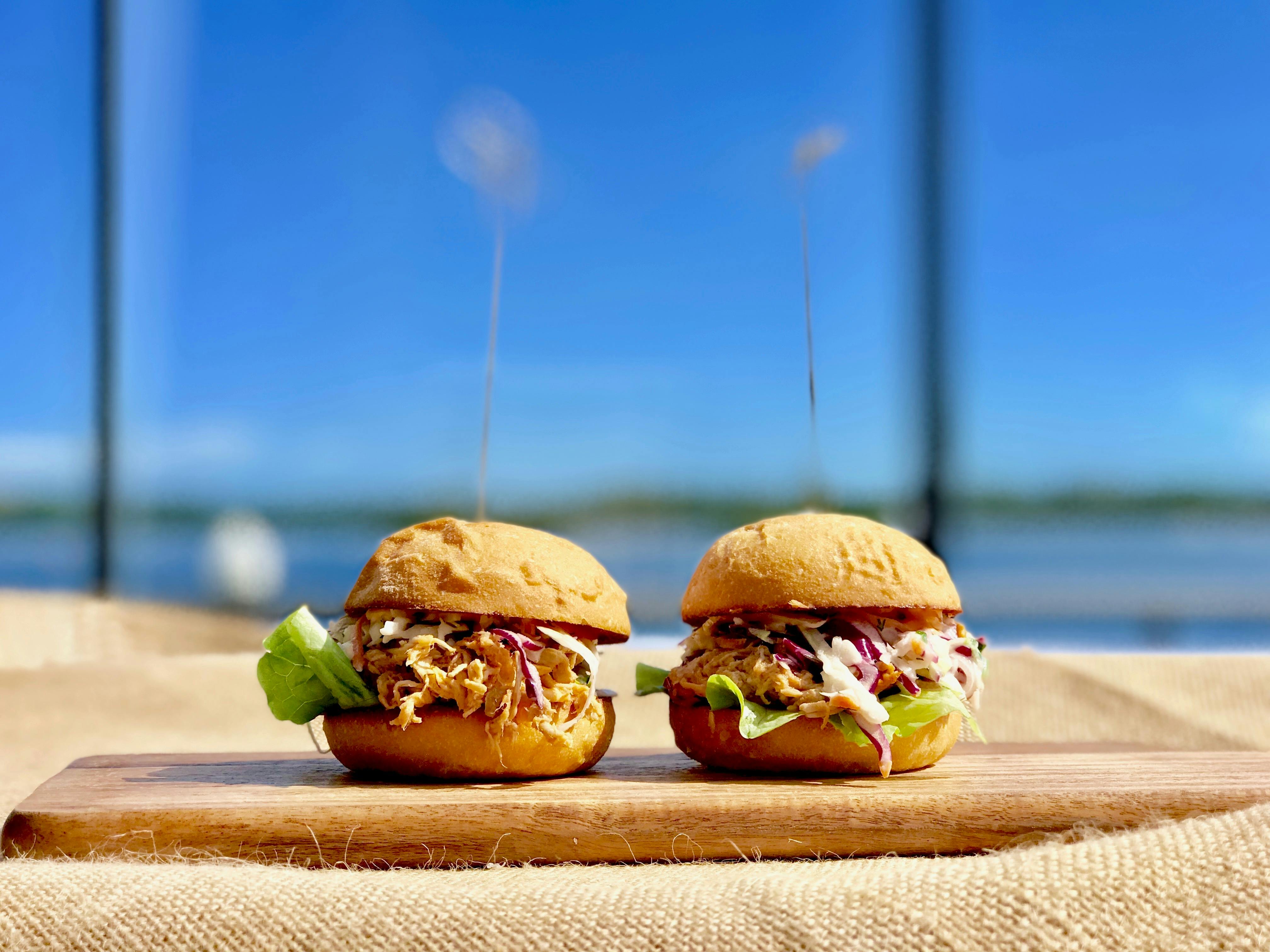 Two pork slider burgers on a board with the river in the background