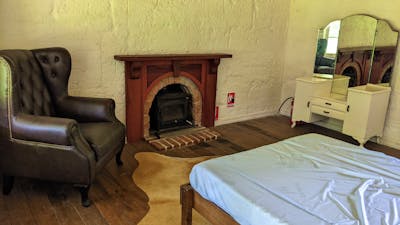 Bedroom with double bed, fireplace, wingback chair and vintage dressing table with mirrors