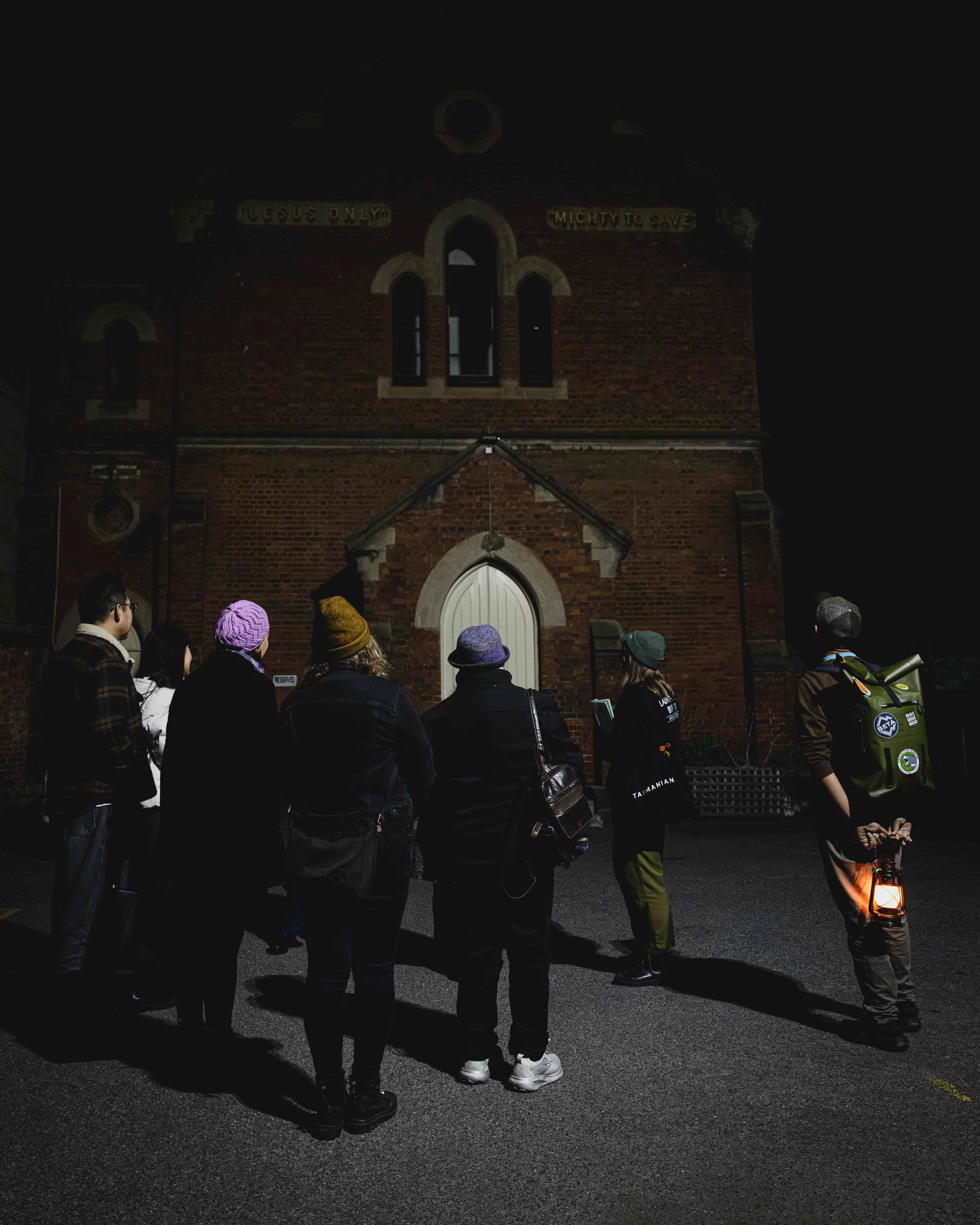 Dark Side of Launceston tour group looking towards a historic church illuminated at night.