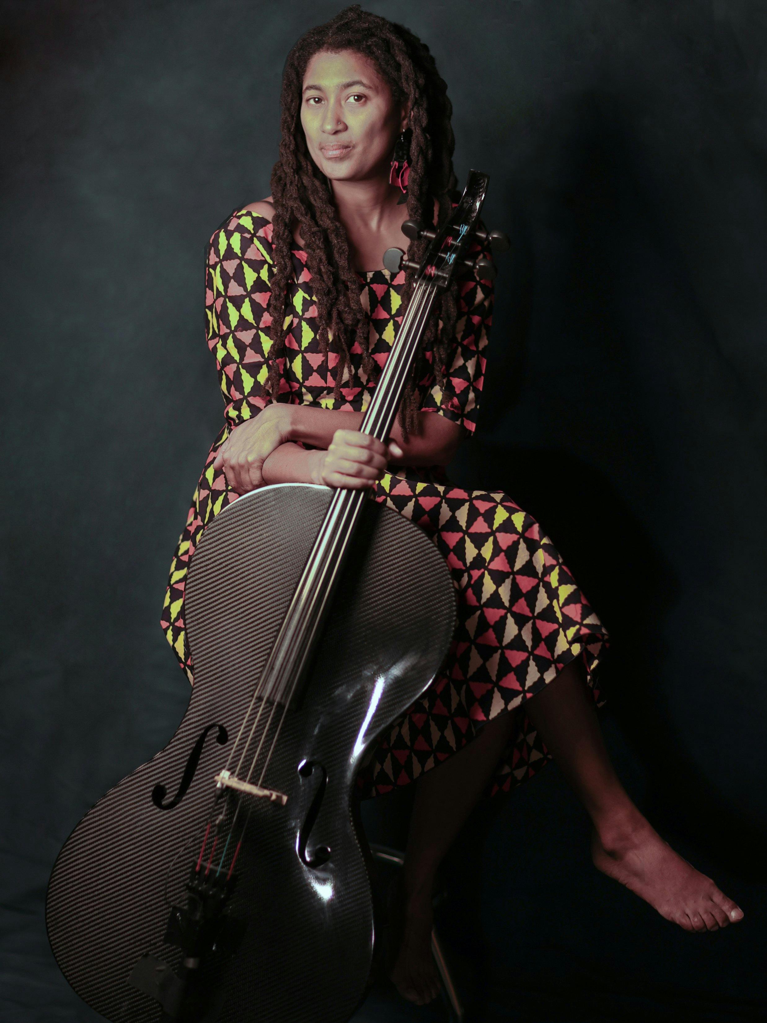 Tomeka Reid, poses in a patterned dress with dreadlocks and her cello