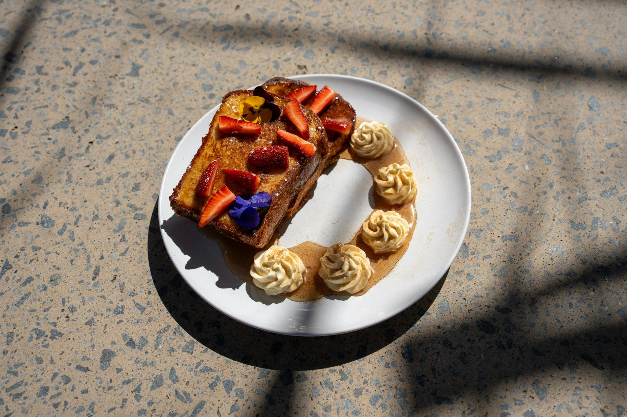 A plate of French Toast with fruit and edible flowers.