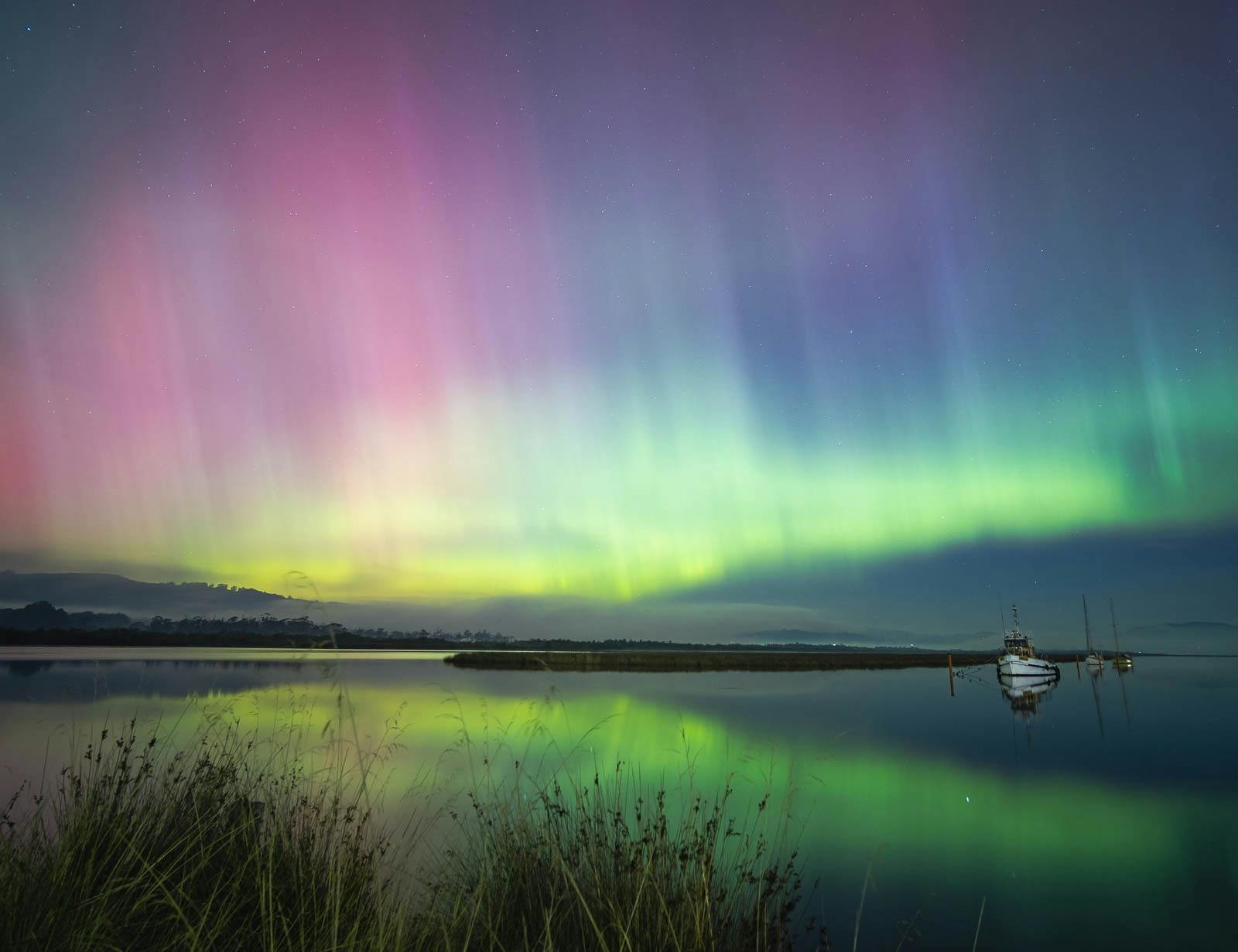Bright aurora reflected in calm water river beneath a clear night sky.