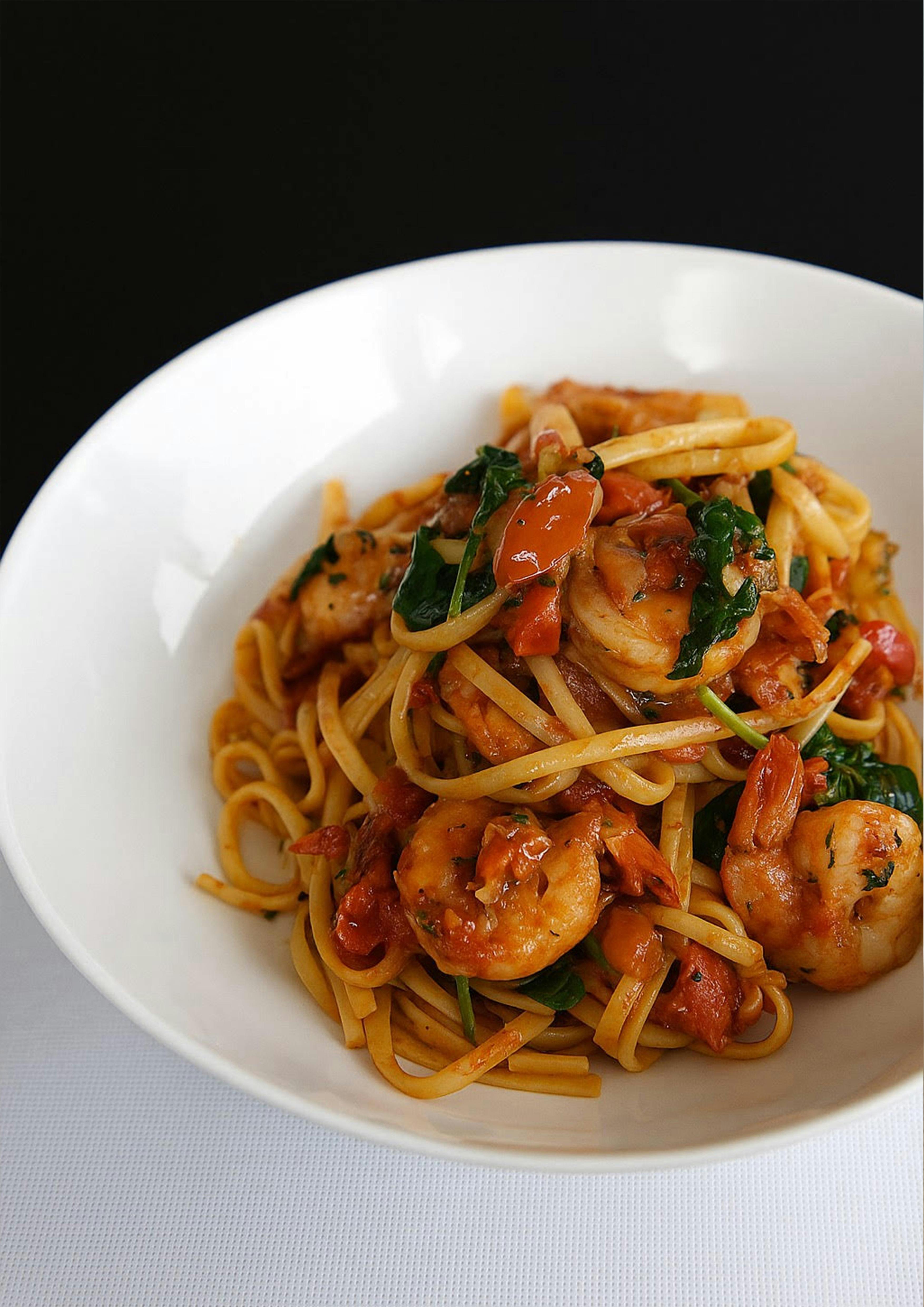 Linguine pasta with prawns, chilli, and fresh herbs in a white bowl at Esteria