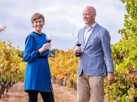 Man and woman smile while drinking red wine in vineyard
