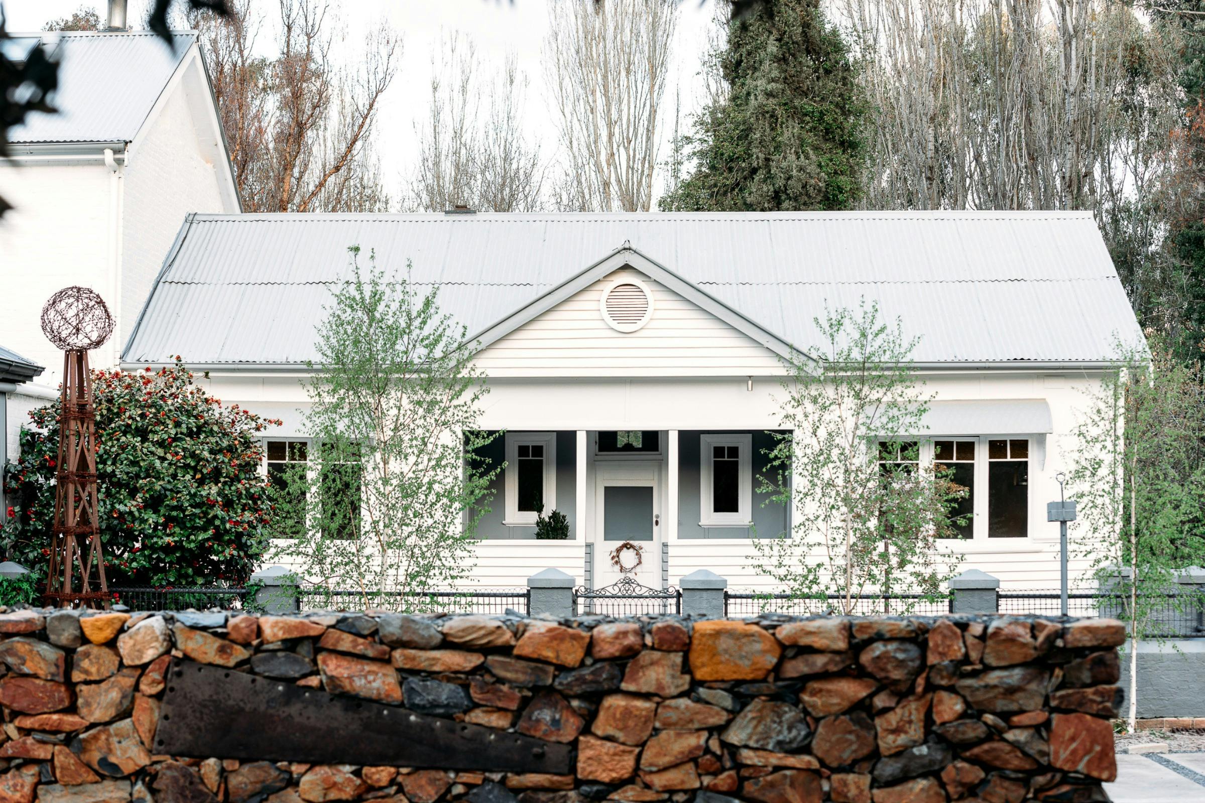 White heritage cottage with a corrugated iron roof, garden and stone wall in Carcoar.