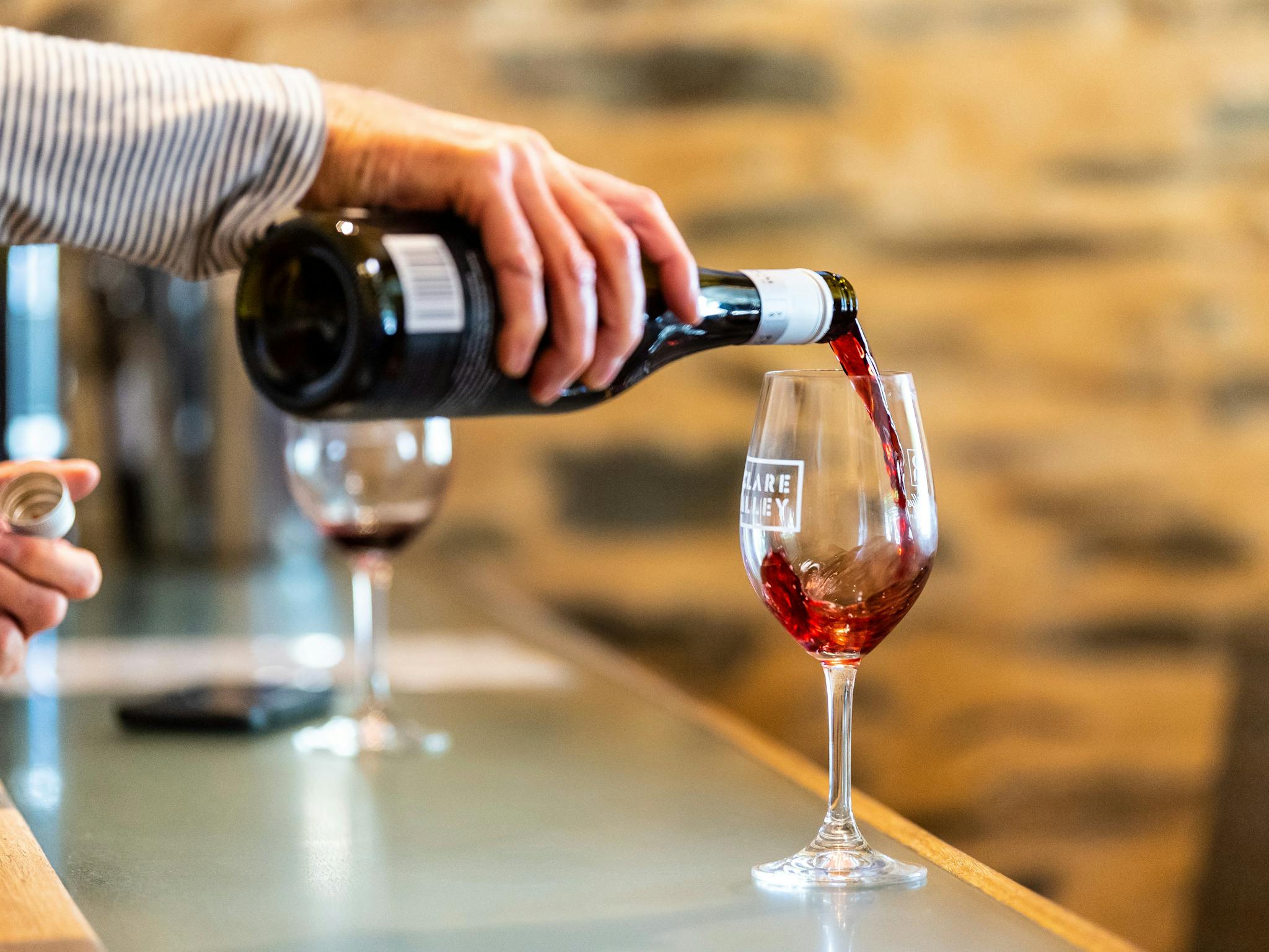 Hand pouring a bottle of red wine into a wine glass that says "Clare Valley"