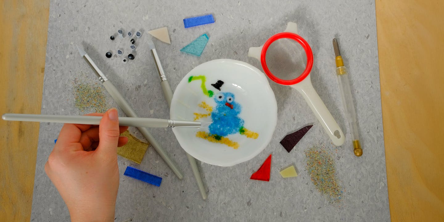 Hand moving glass frit around a design for a kilnformed bowl. With all the tools surrounding