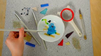 Hand moving glass frit around a design for a kilnformed bowl. With all the tools surrounding