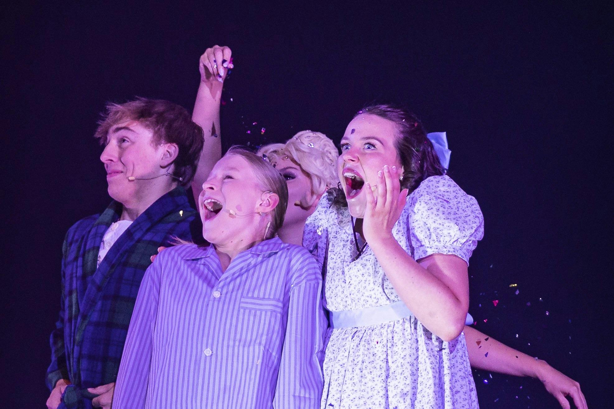 Peter Pan cast members dressed as the Darling children looking up in wonder on stage