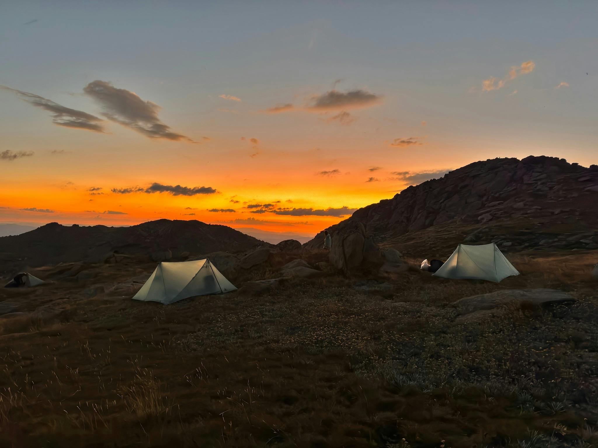 Two tents set up in the mountains with the sun setting behind them.
