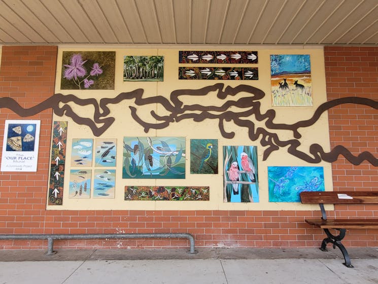 Metal Murray Rover sculpture on a yellow wal with small individual artworks depicting native scenes