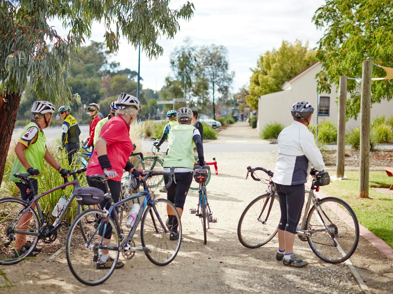 A number of cyclists on the footpath buildings cars trees shrubs in background at Glenrowan