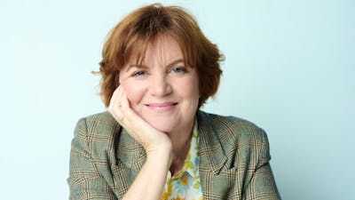 Woman smiles at camera leaning her chin on her hand