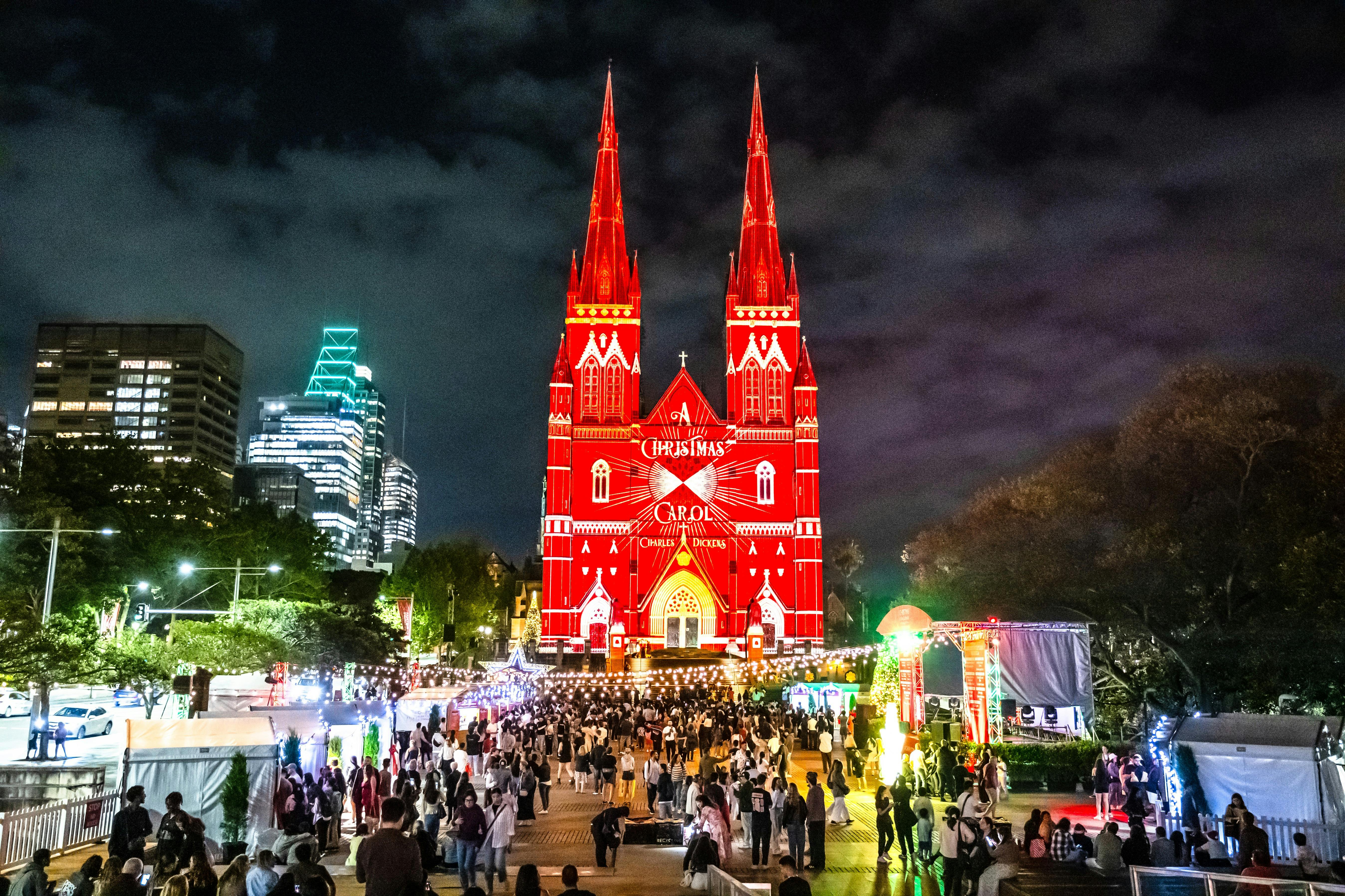 A vibrant crowd fills the forecourt as St Mary’s Cathedral glows in striking red light projection