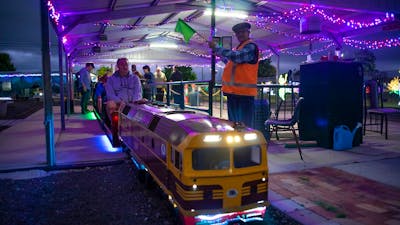 Miniature train at the station under lights with station master signaling to proceed