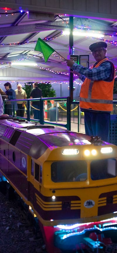 Miniature train at the station under lights with station master signaling to proceed