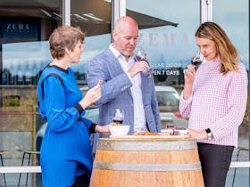 three people eat cheese and drink wine at winery