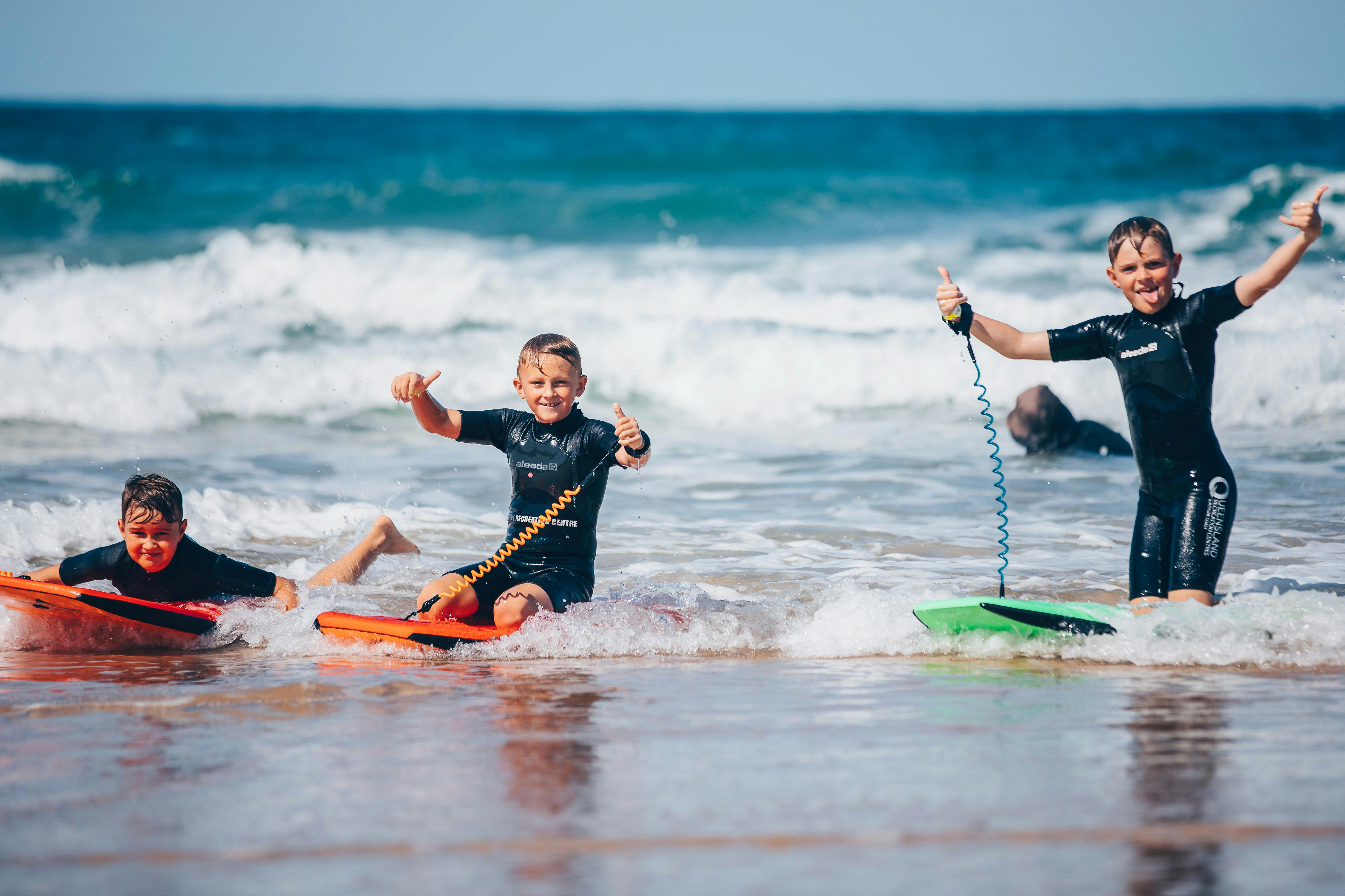 Three children celebrating surfing a wave on a body board