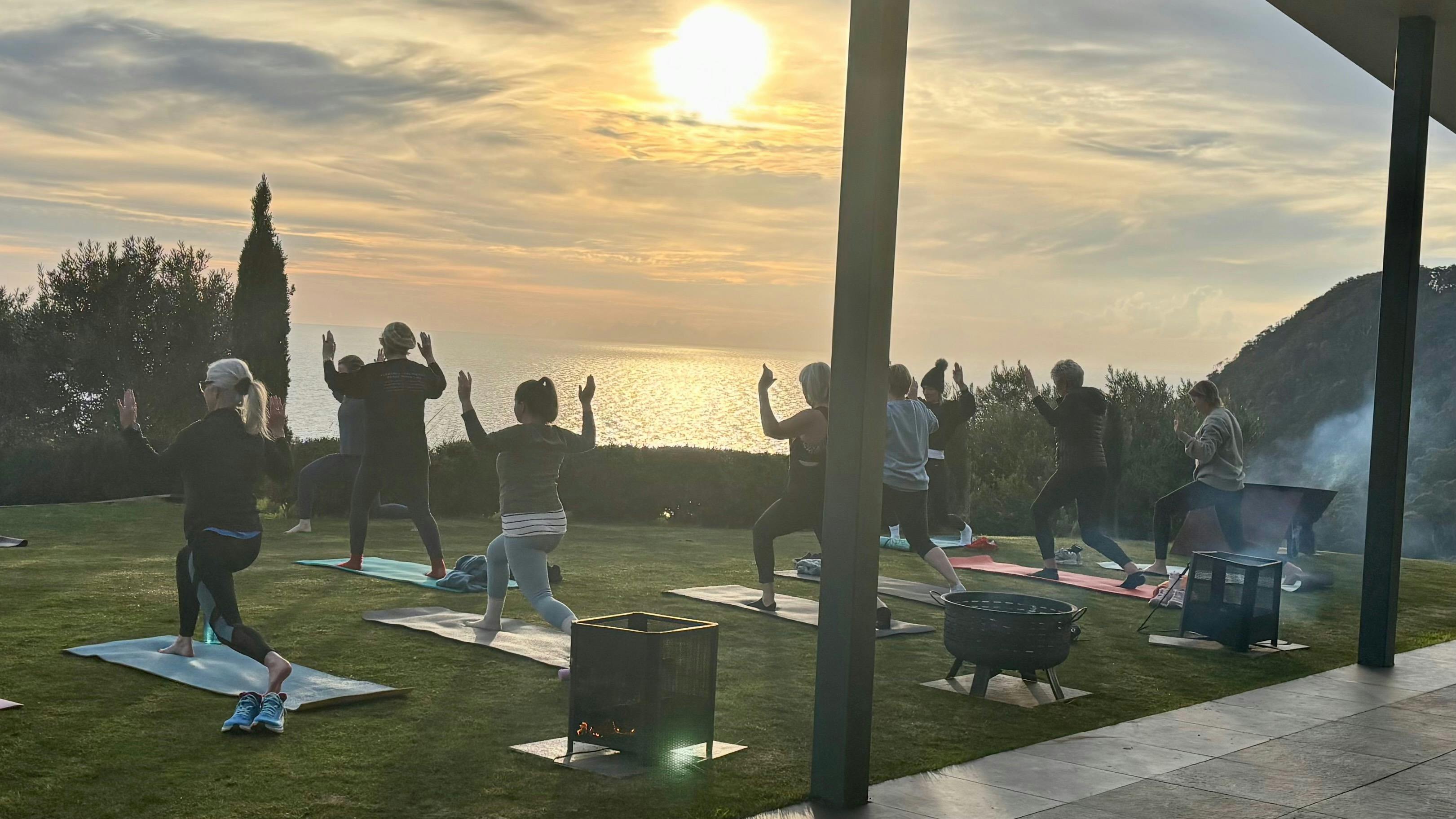 Group of ladies participating in class, surrounded by fire pits at sunrise