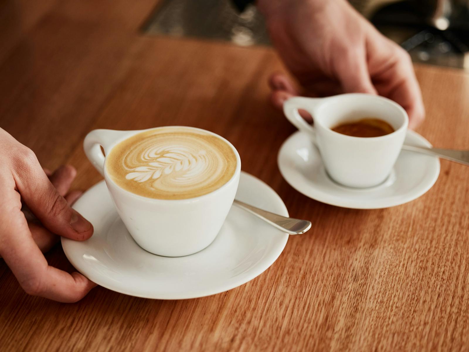 Hands placing two coffees on a counter.