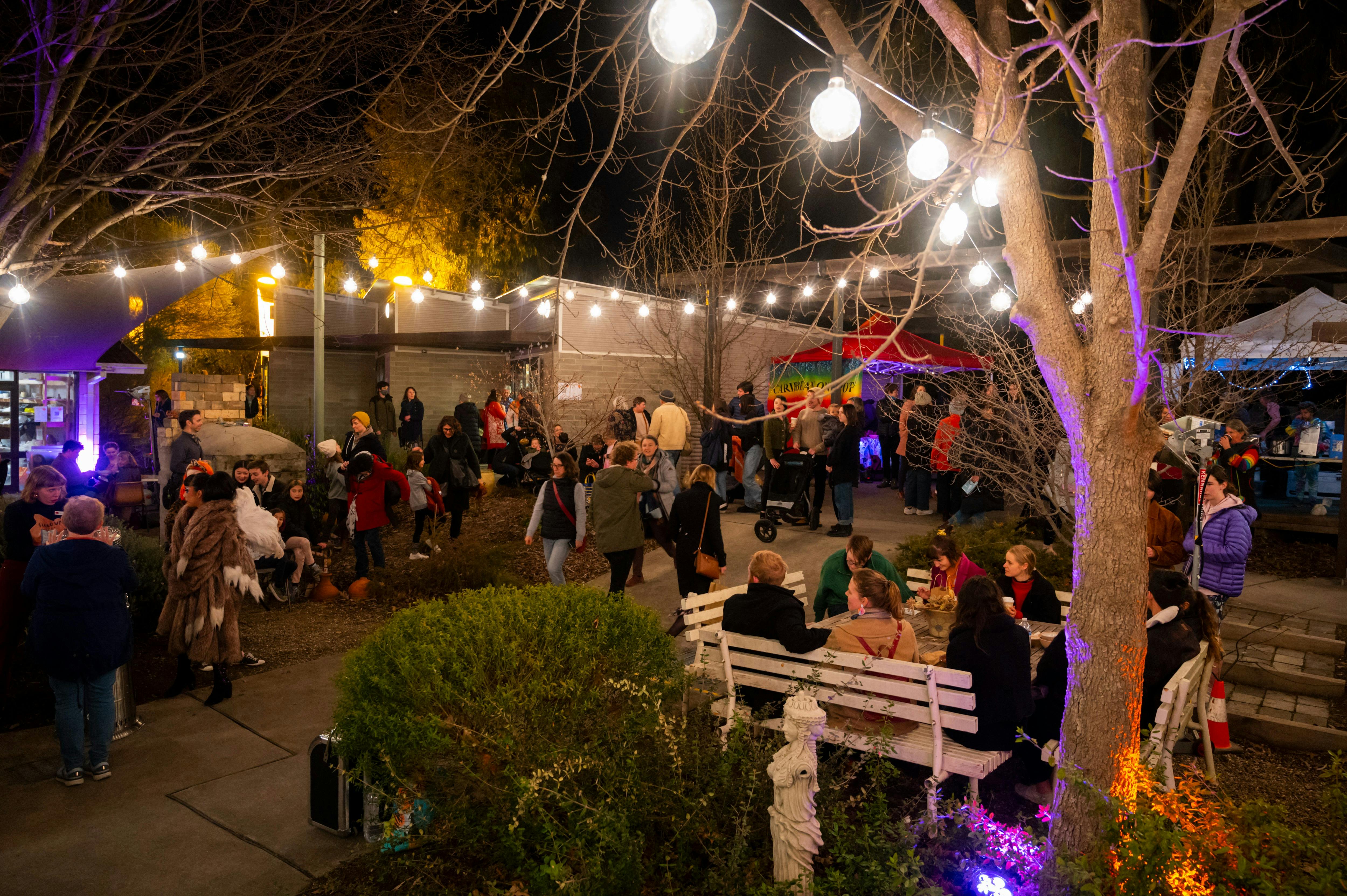 Canberra Potters courtyard at night, with crowds of people and bright coloured and festoon lighting