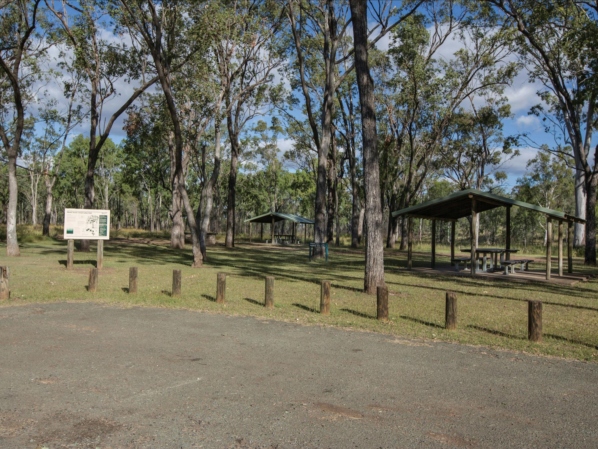 Picnic tables under shelters in woodland.