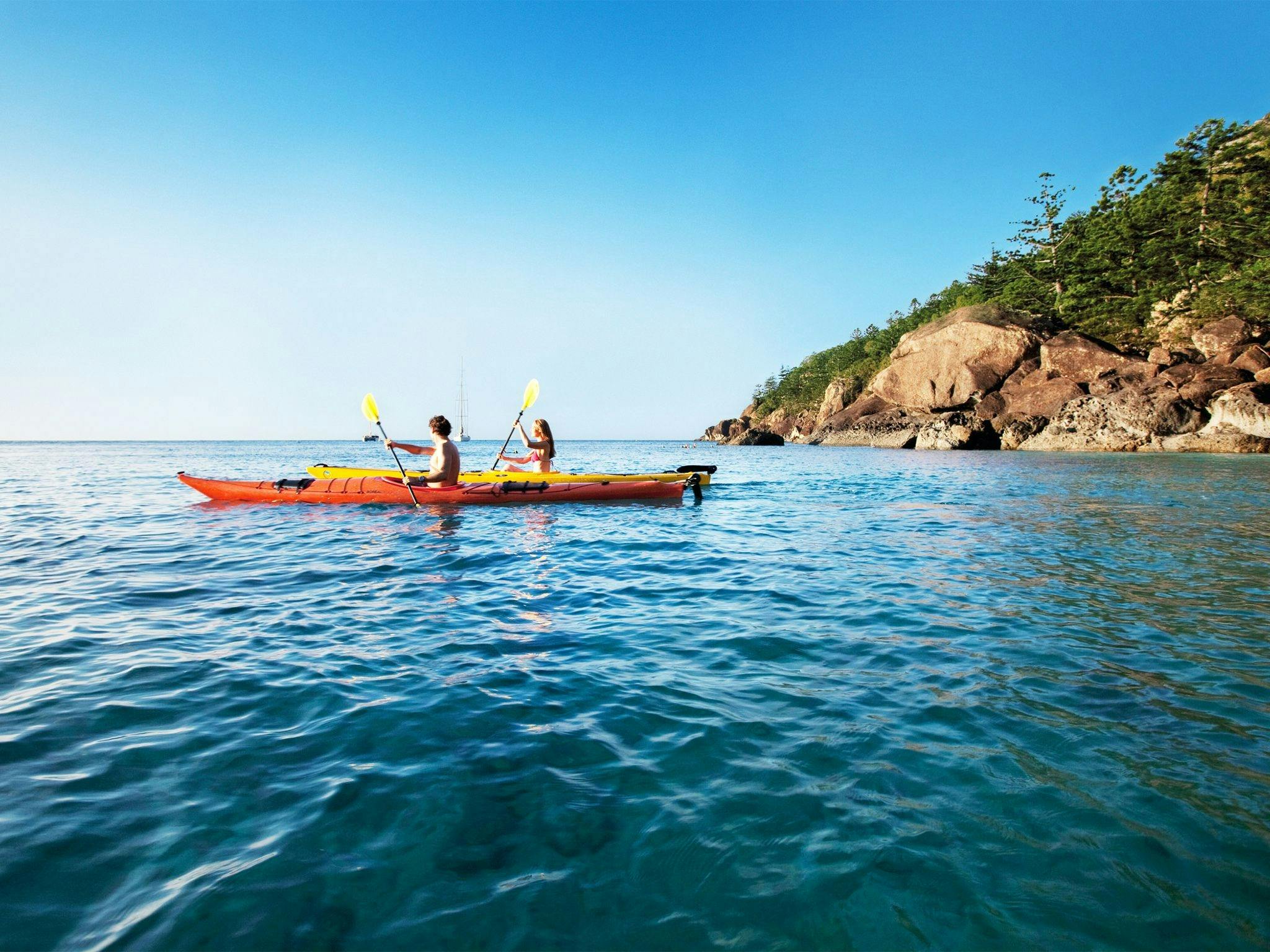 Two people in orange and yellow kayaks with an island in the background.