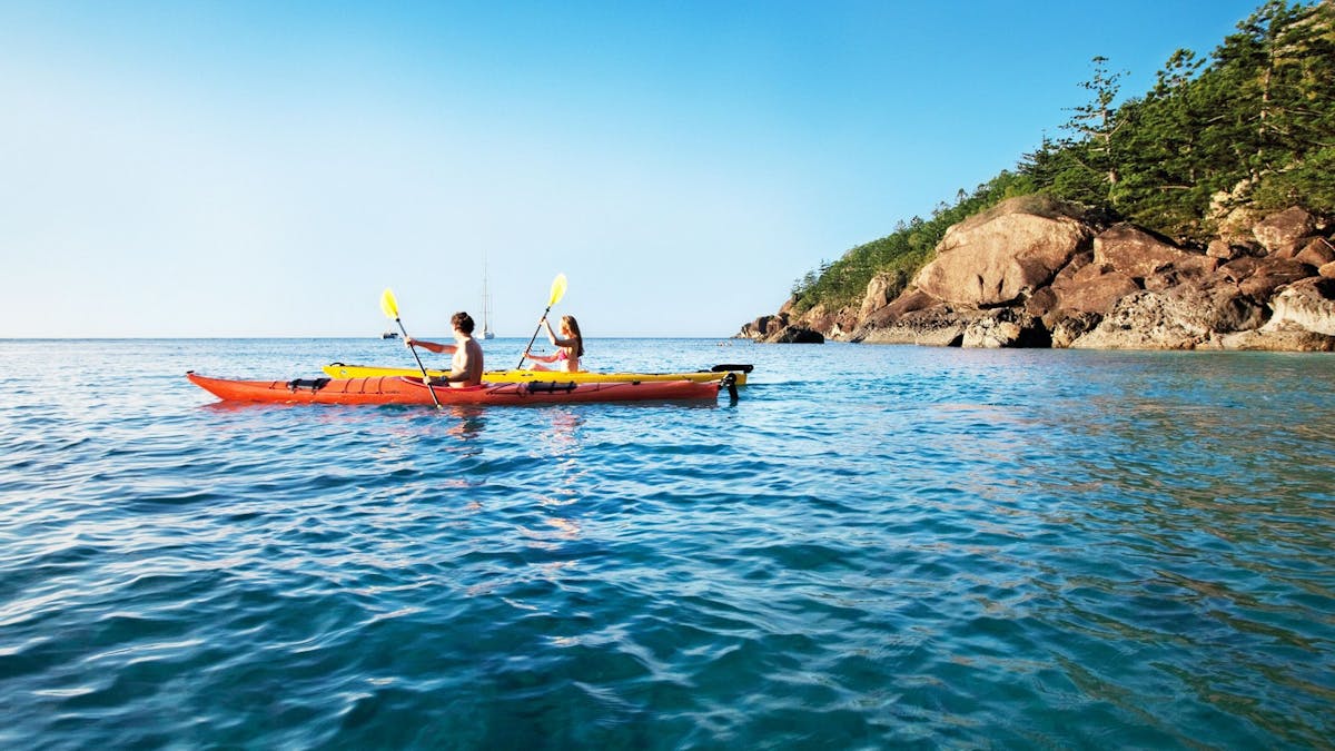 Two people in orange and yellow kayaks with an island in the background.