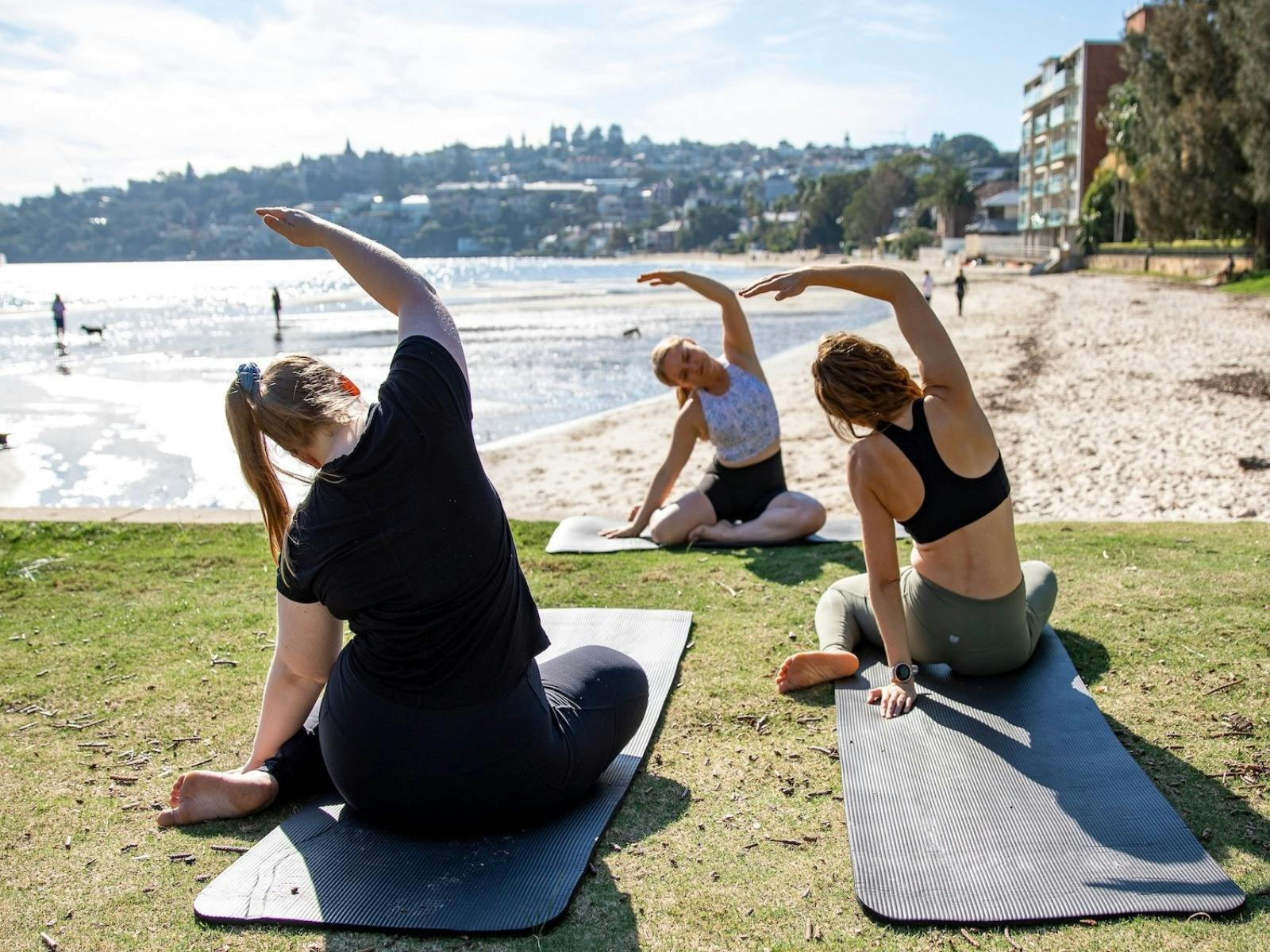 Group practicing pilates on mats beach in background