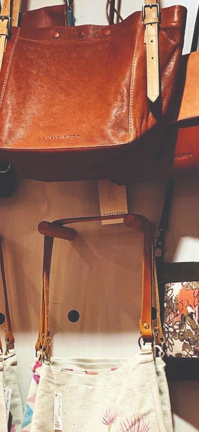 Leather handbags hanging on a pegboard display with printed linen totes