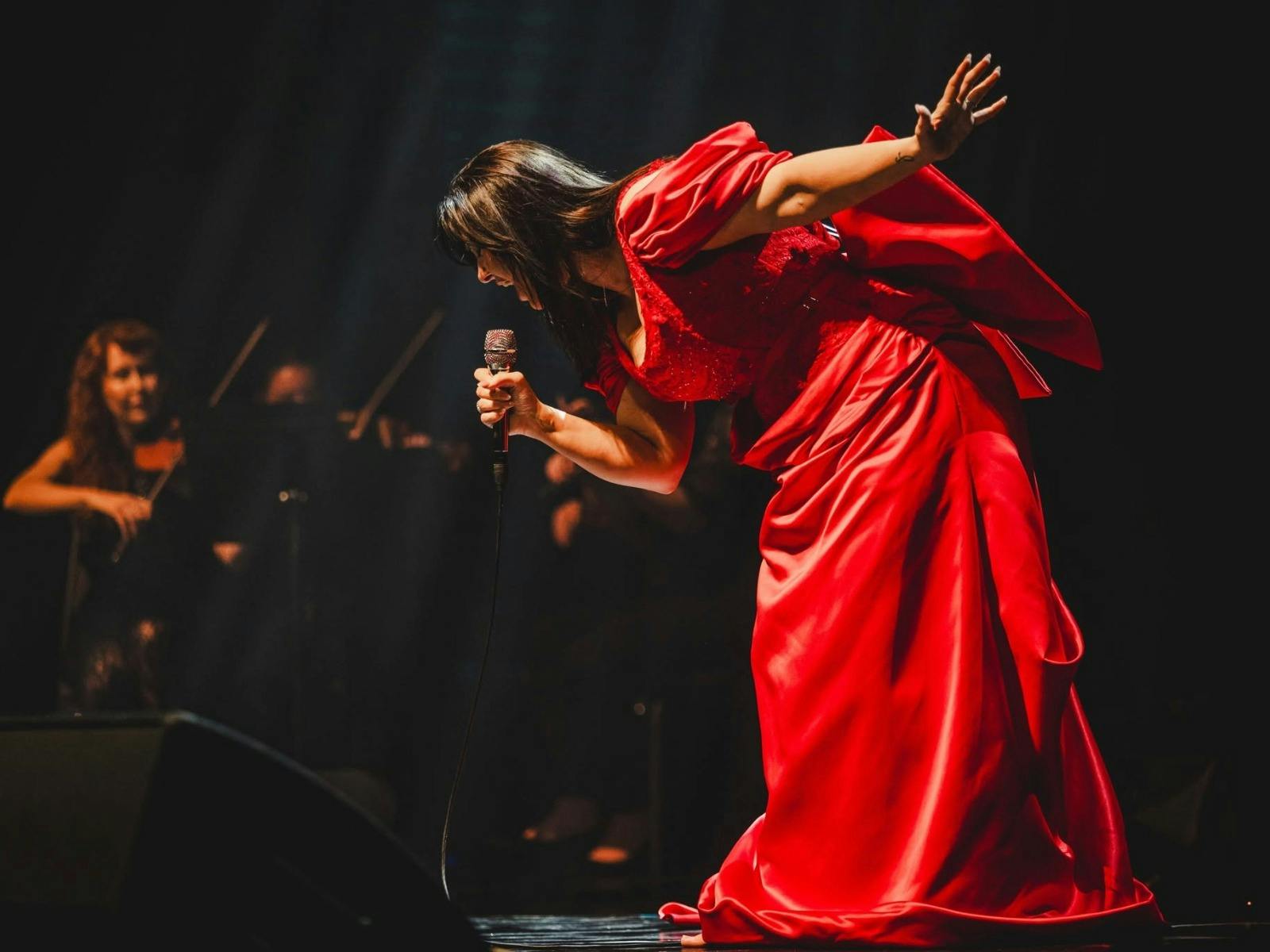 lady wearing a beutiful red dress is singing on stage