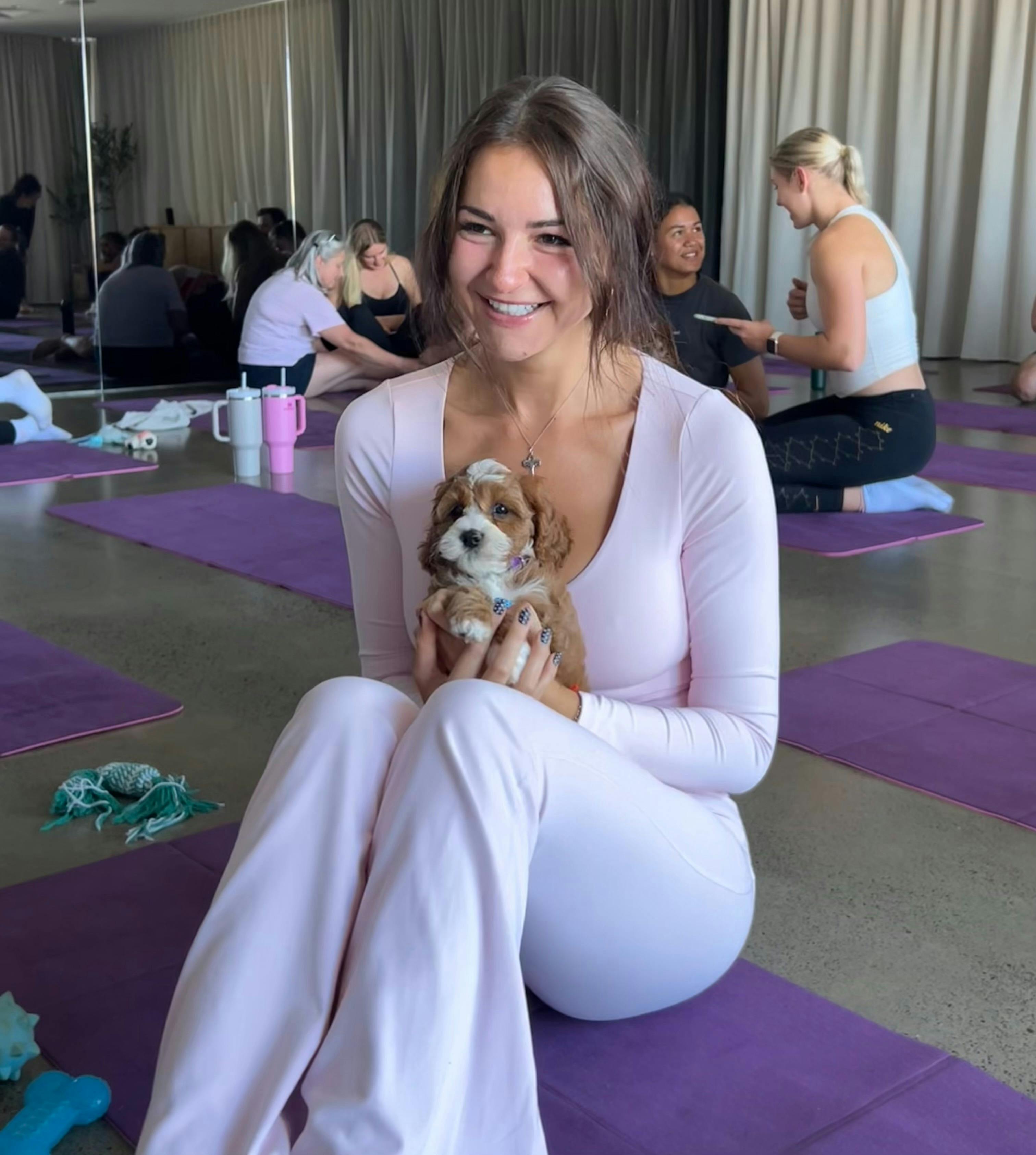A participant relaxes on a purple mat with a puppy during Puppy Yoga Brisbane with Yoga Paws.