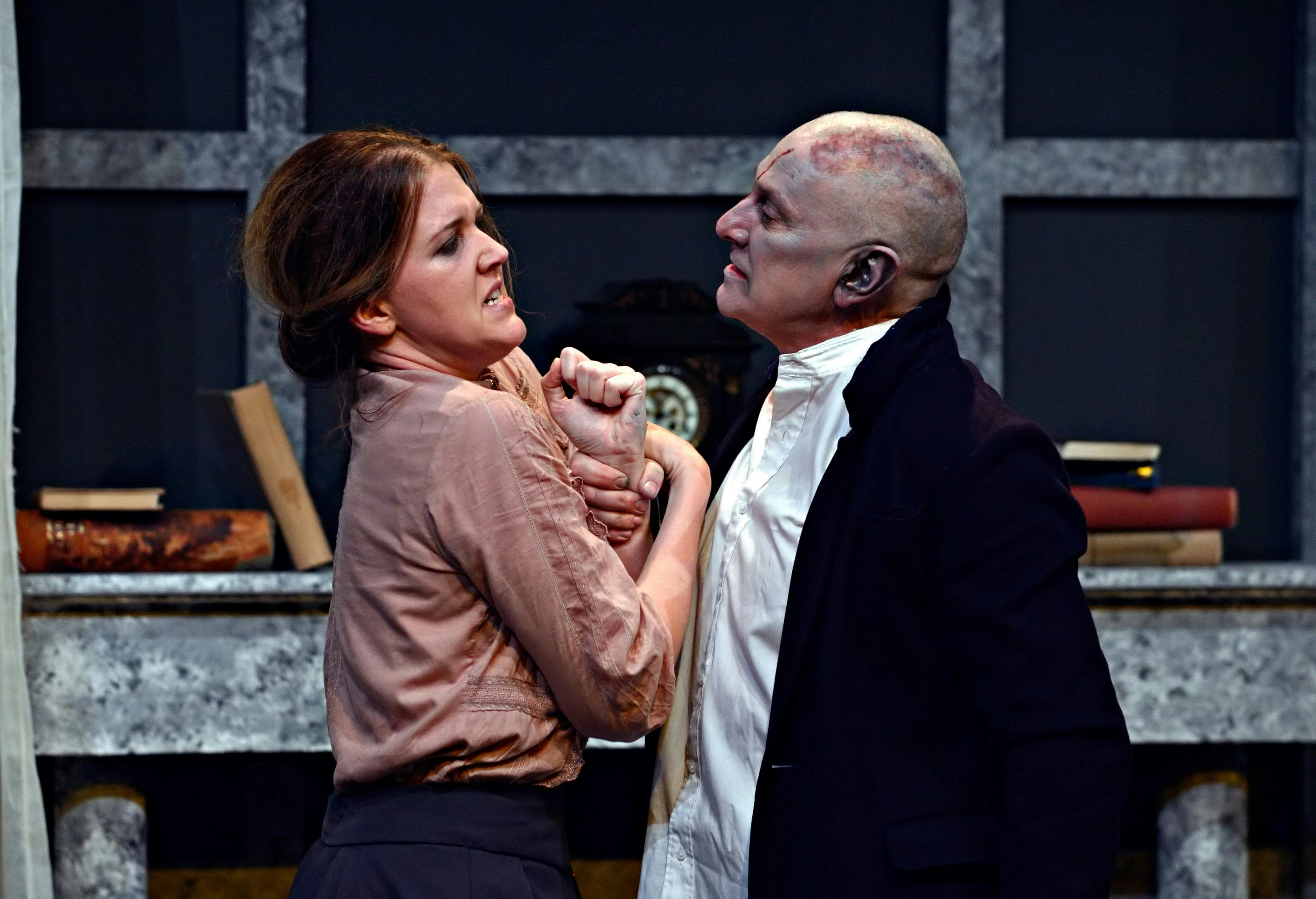a young woman in loose fitting shirt is in the grip of a bald, suited man - Frankenstein's monster