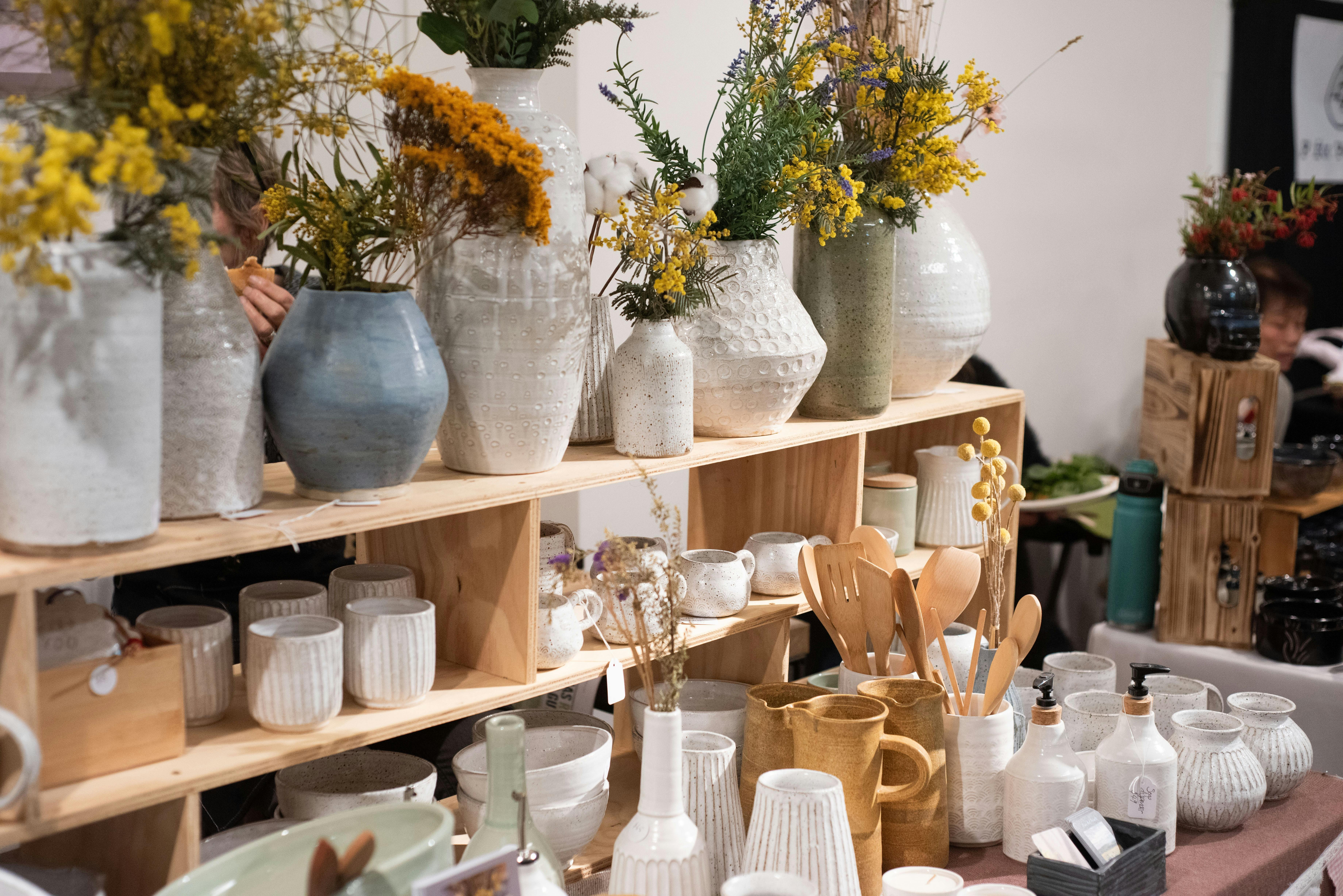 A market stall with shelves of white and pale blue/green pottery. Some pots have flowers.