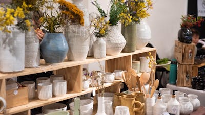 A market stall with shelves of white and pale blue/green pottery. Some pots have flowers.