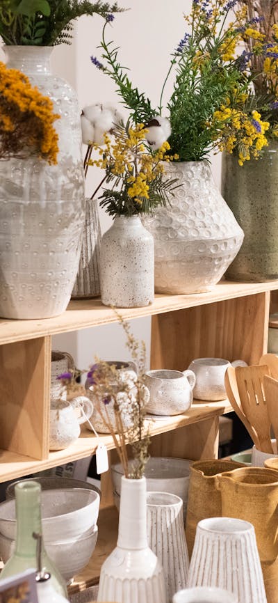 A market stall with shelves of white and pale blue/green pottery. Some pots have flowers.