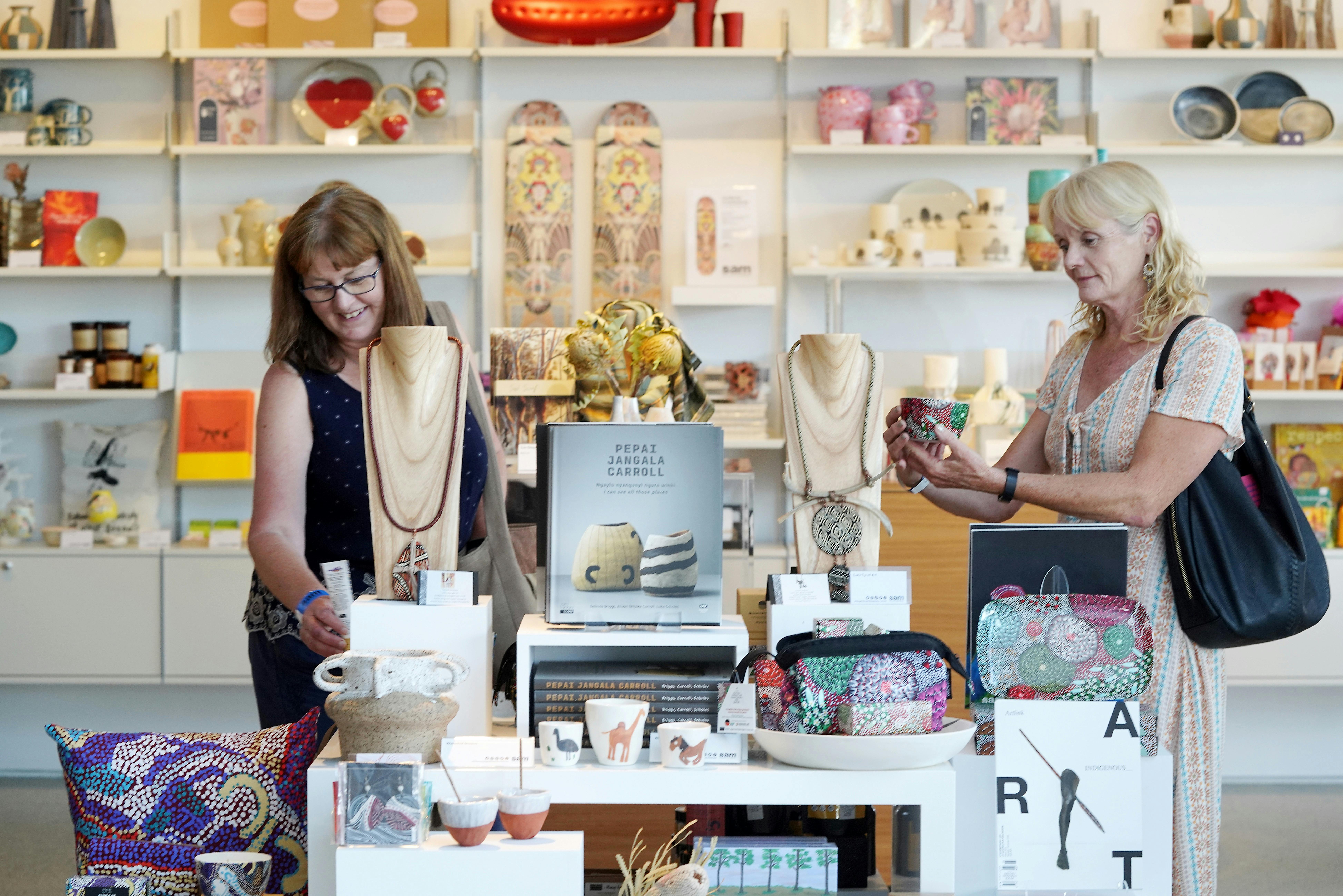 Two women browse a display table holding ceramics and books in a museum shop