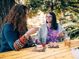 Two women eating morning tea at cafe with drinks looking at each other smiling