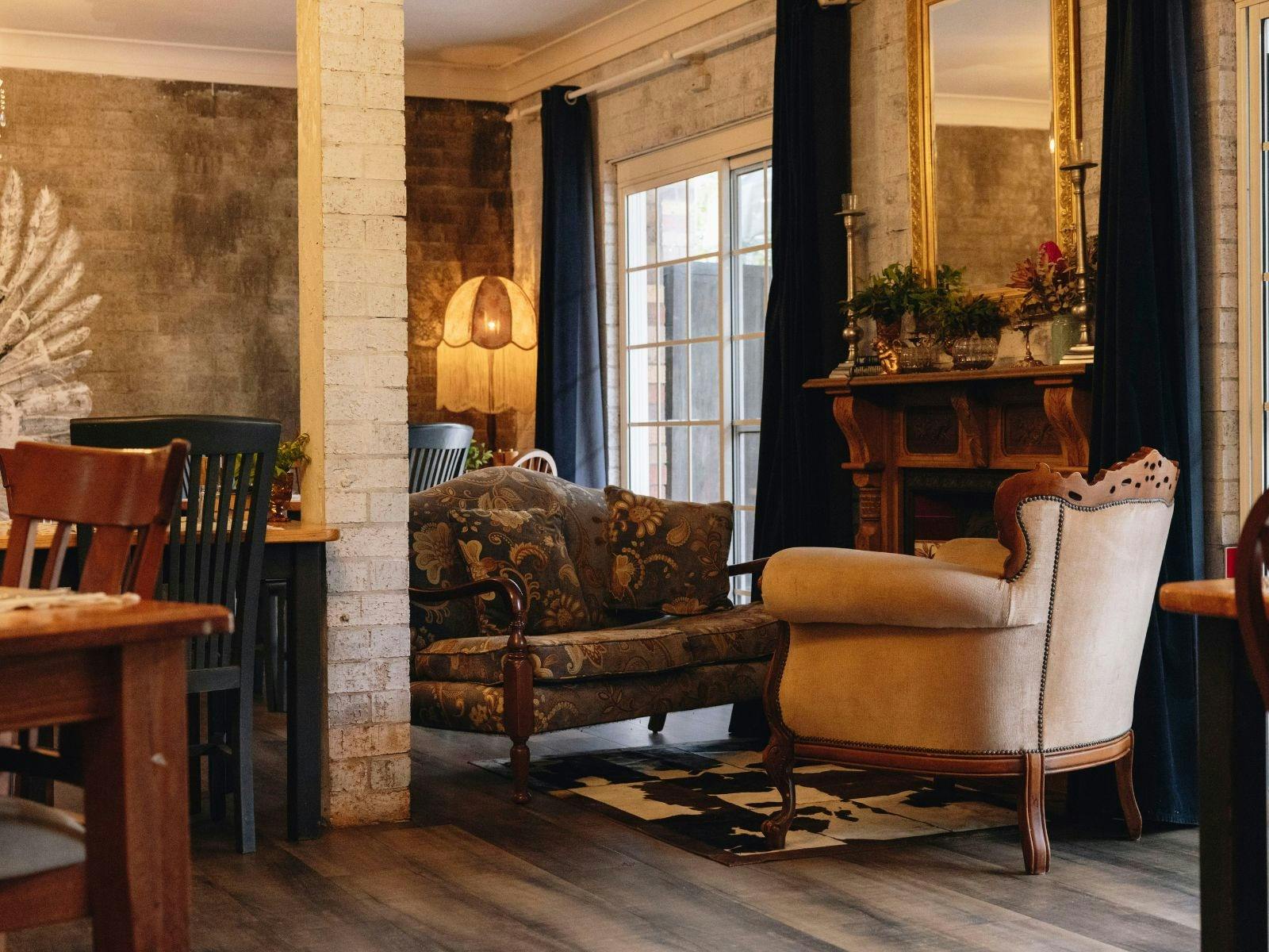 Cozy vintage lounge with patterned sofa, armchair, fireplace, and large window with curtains.